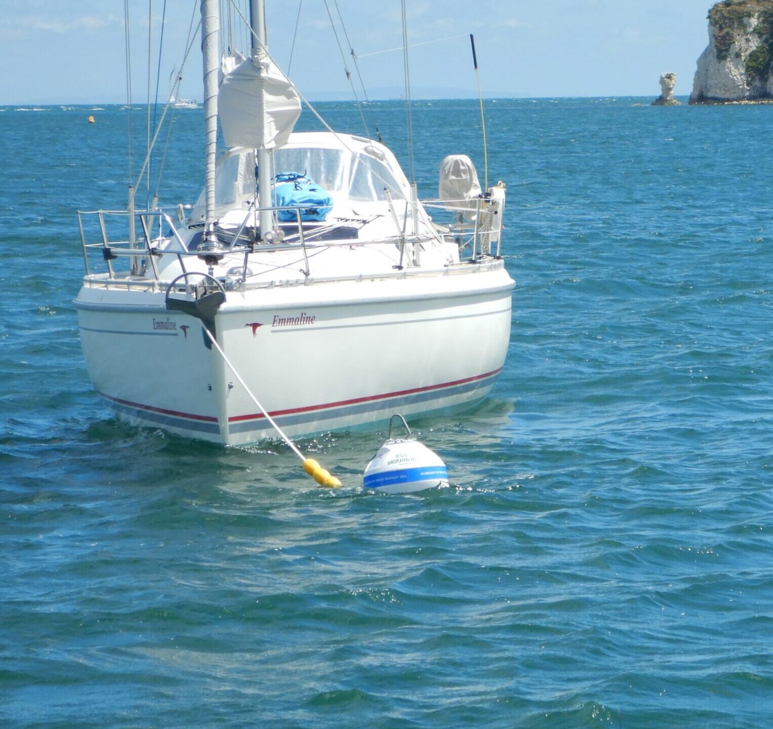 White boat attached to an eco-mooring in the sea. Old Harry Rocks, a famous rock formation, in the background.