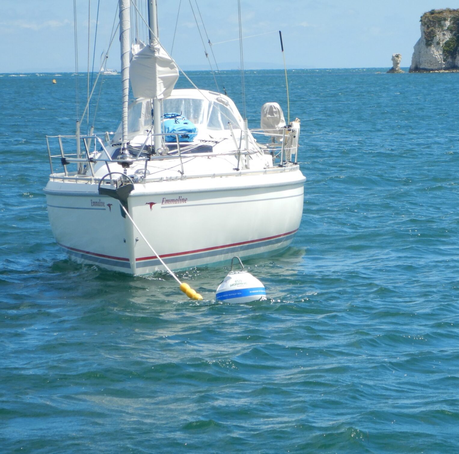 White boat attached to an eco-mooring in the sea. Old Harry Rocks, a famous rock formation, in the background.