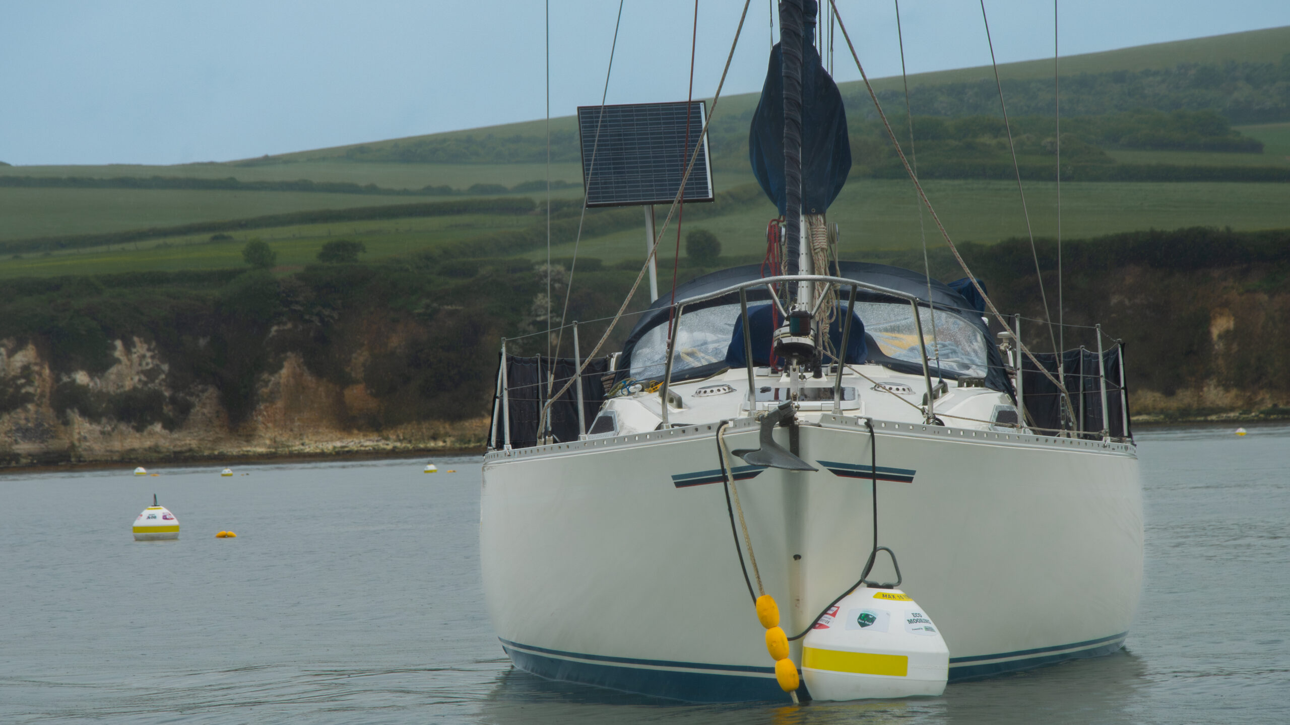 A white boat attached to an eco-mooring, Ballard Down in the background.