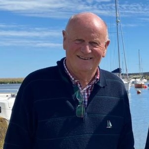 Jim Atkins photographed by a marina with sea and boats behind him.