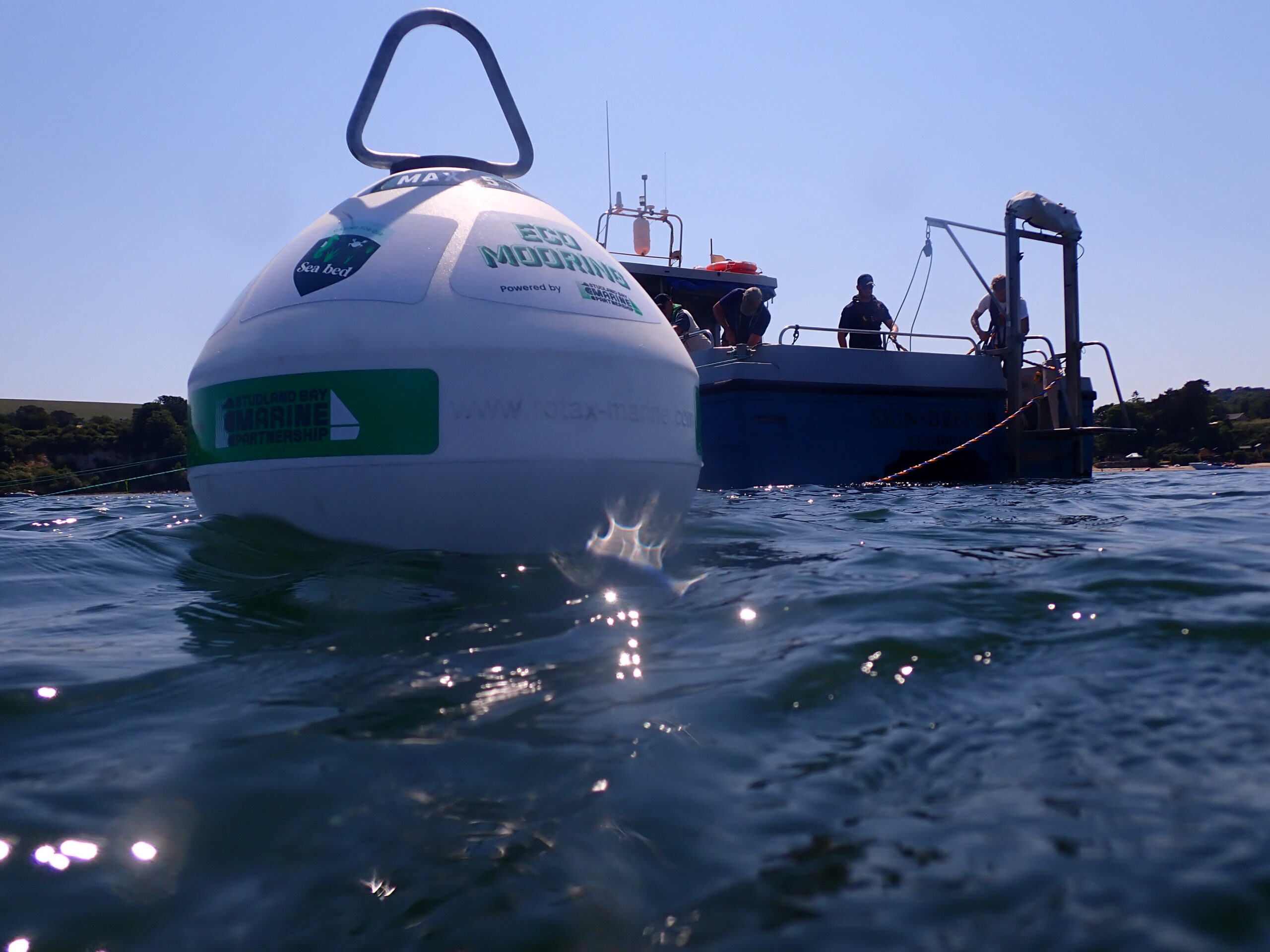 Eco-mooring buoy in the foreground with a boat behind, and several people helping install it.