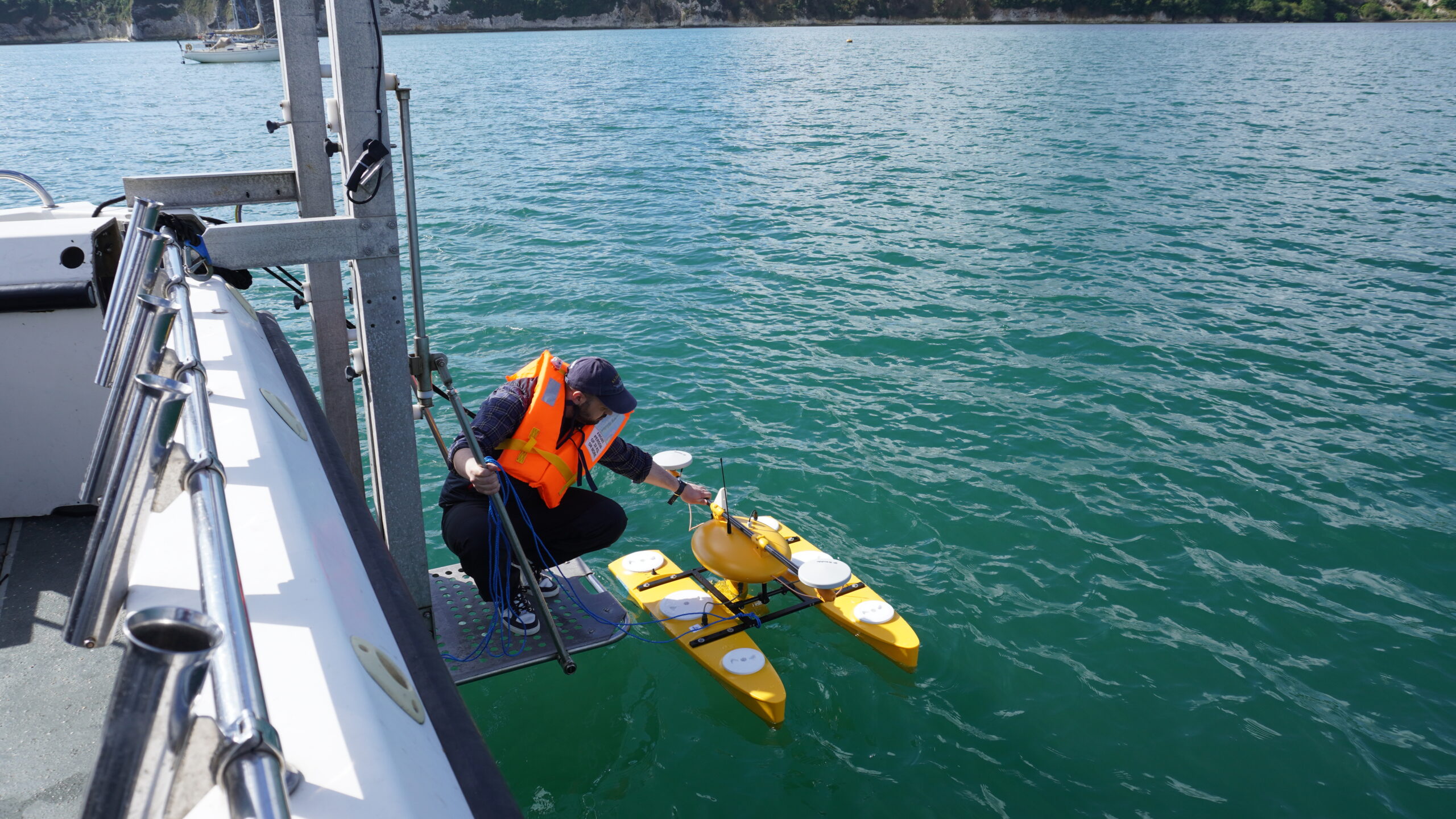 A yellow remotely operated boat being launched off the side of a vessel by a research scientist.